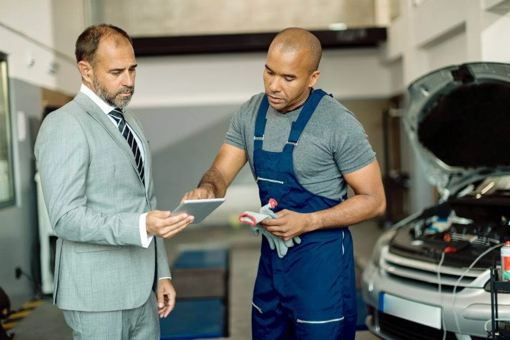 Black mechanic and his manager working on touchpad in auto repair